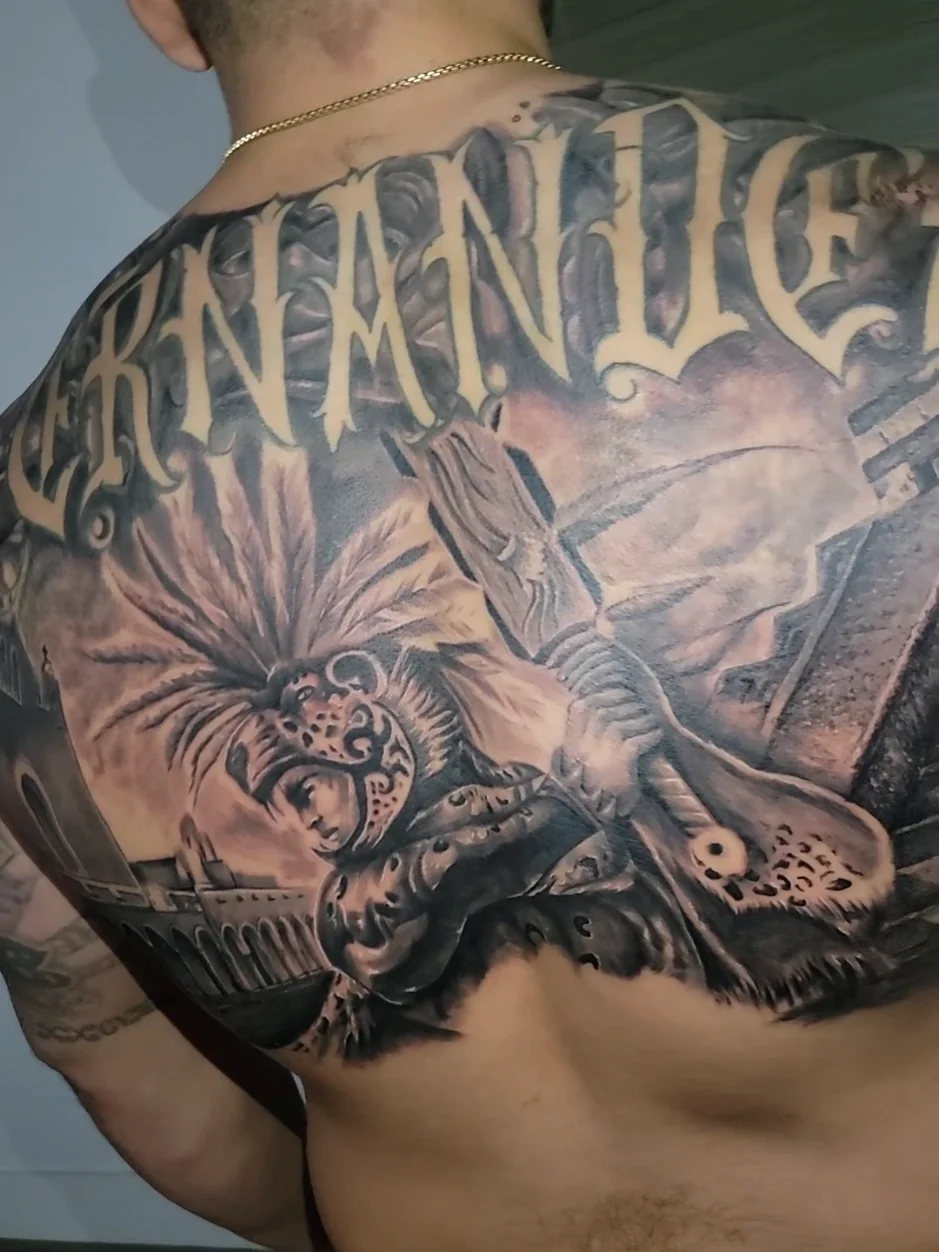 Aztec warrior with feathered headdress and HERNANDEZ lettering back tattoo by Alex Zamora