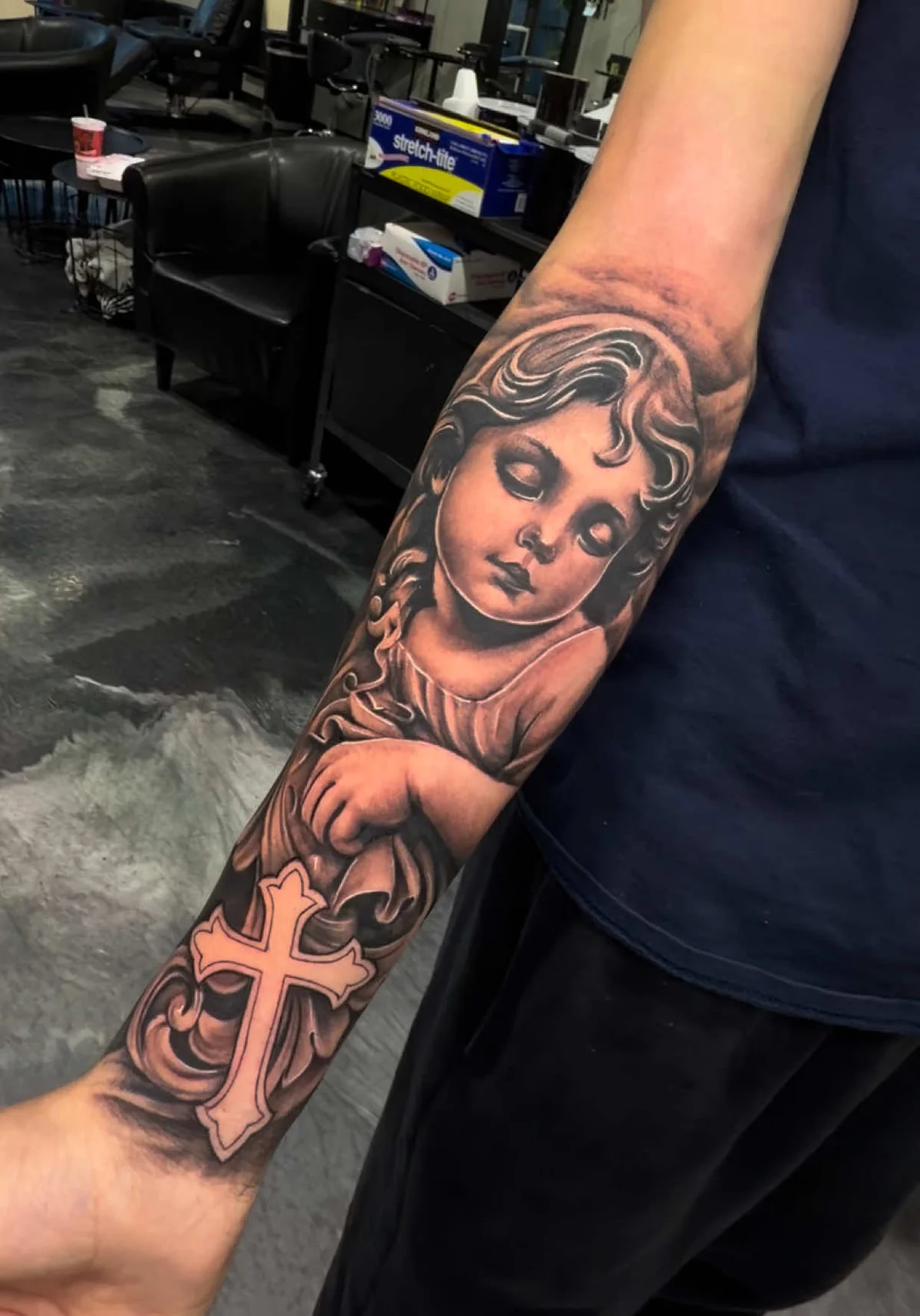 Cherub with cross religious tattoo on forearm by Alex Zamora